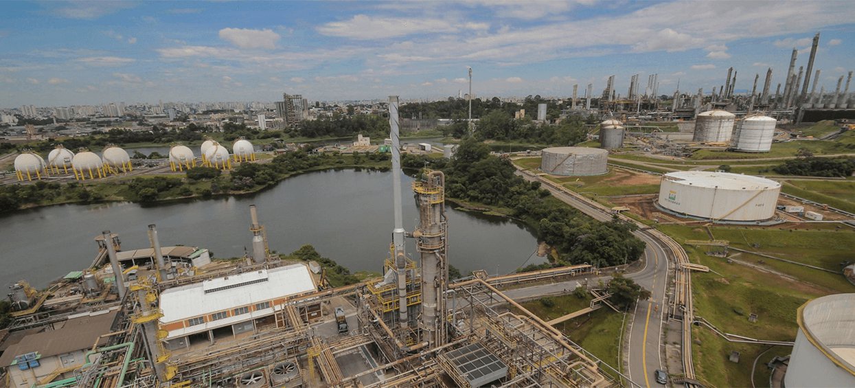 Foto aérea de refinaria da Petrobras. Ela possui uma lagoa no centro.