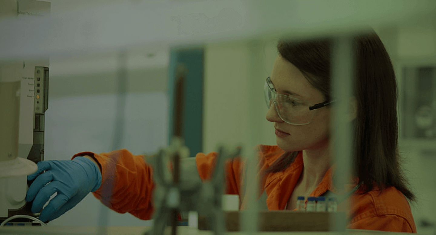 Funcionária com carreira na Petrobras, usando uniforme, e óculos de proteção fazendo testes químicos.