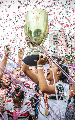 mulher levantando uma taça de campeonato de futebol com papel picado ao fundo