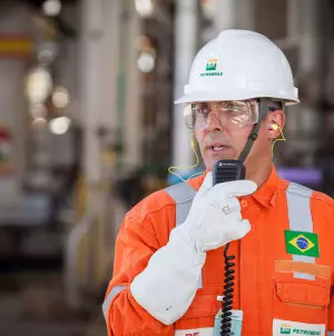 Funcionário da Petrobras usando equipamento de proteção individual completo e falando a um walkie talkie.