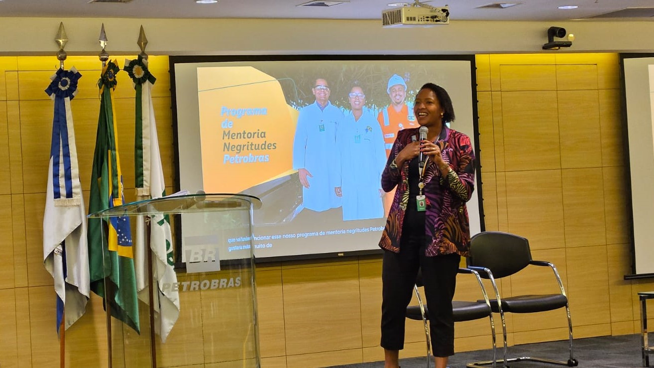 Mulher negra com um microfone em mãos, dando uma palestra.