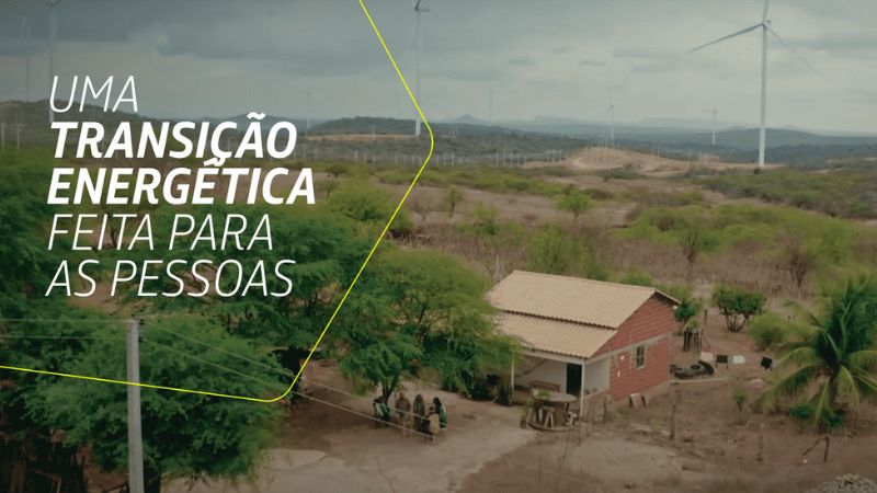Imagem de uma área rural com turbinas eólicas ao fundo e uma casa simples à frente. Texto: 'Uma transição energética feita para as pessoas'.