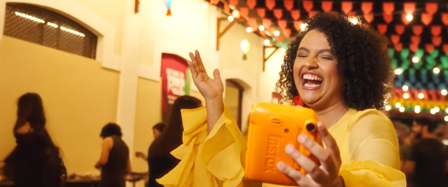 Influenciadora Amora, uma mulher negra de cabelos crespos, dança e sorri em uma festa junina, com bandeirolas penduradas.