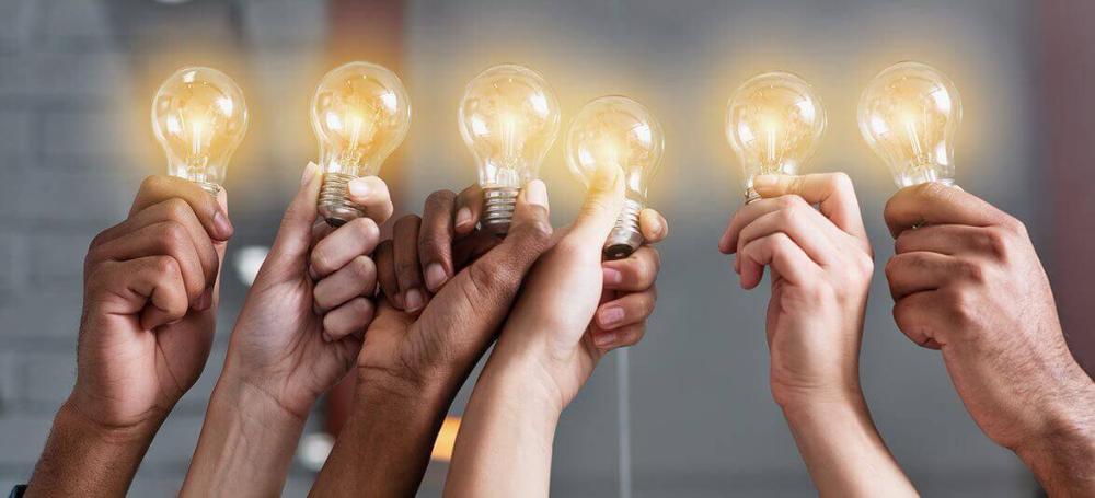Seis mãos levantadas, segurando lâmpadas representando inovação aberta.