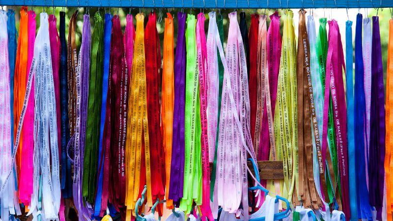 Fitas coloridas do Senhor do Bonfim penduradas lado a lado, cada uma com o texto 