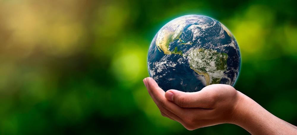 Pessoa segurando globo terrestre na mão com natureza ao fundo. Representa a transição energética.